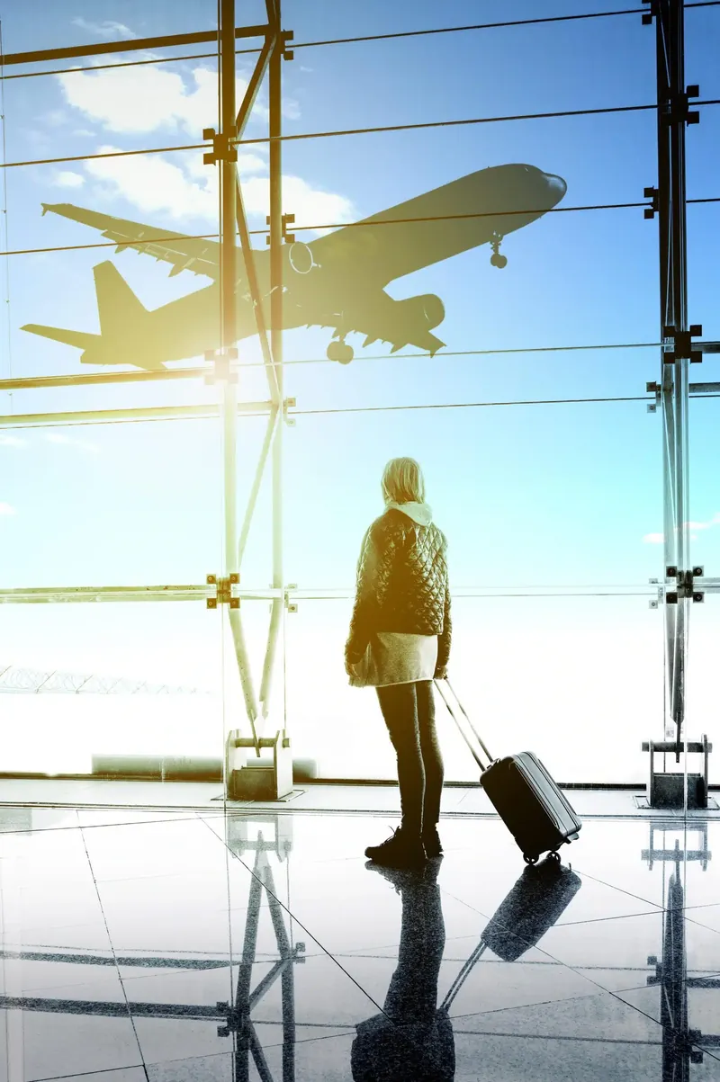 Traveller with a suitcase watching a plane take off from the terminal window