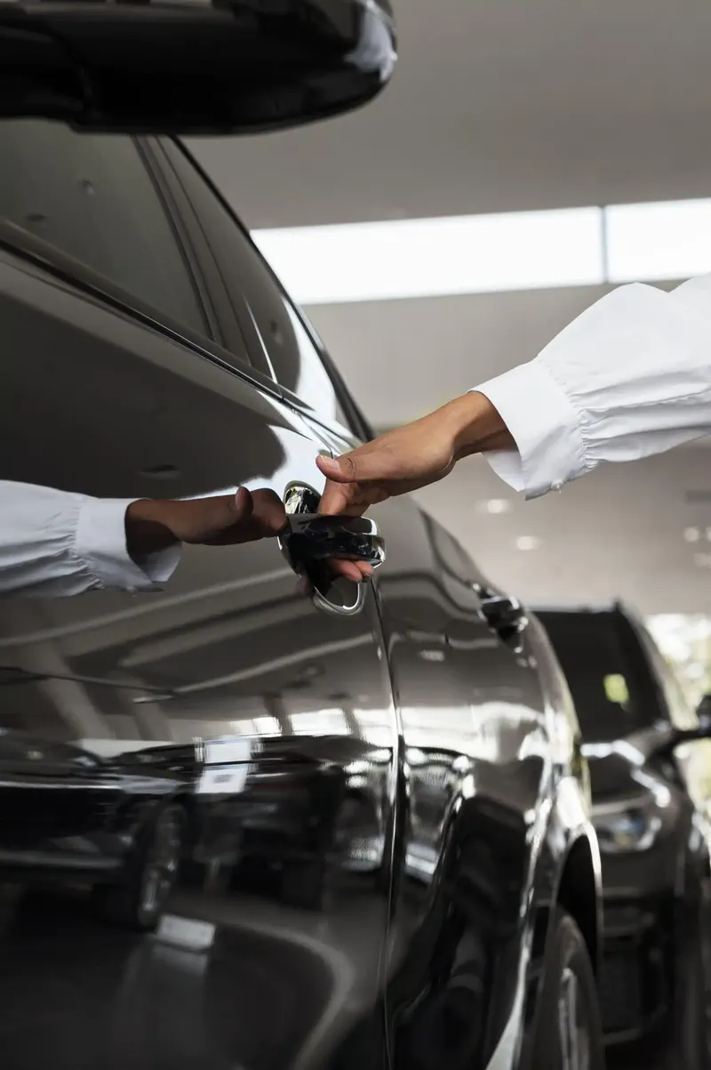 Hands meeting at the door handle of a black rental car